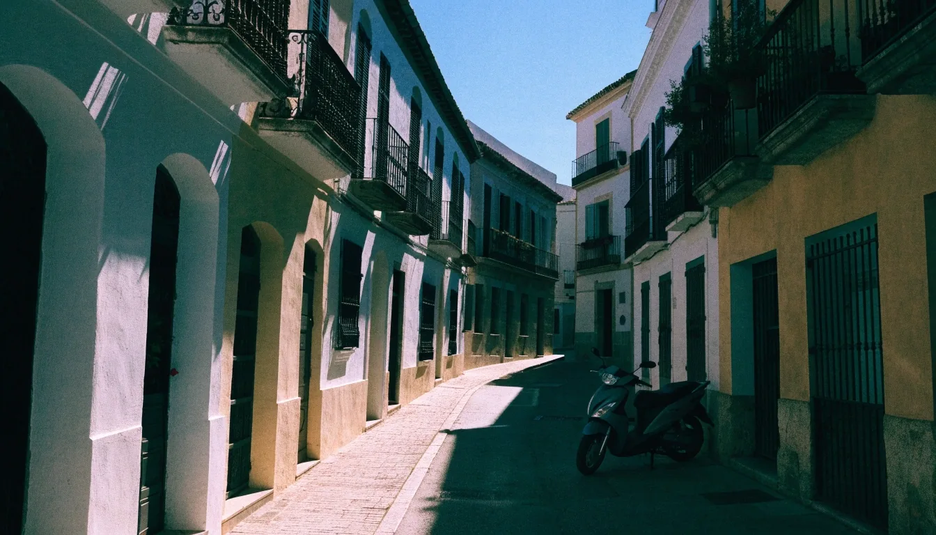 Calle residencial andaluza a media tarde, con fachadas encaladas y balcones de forja